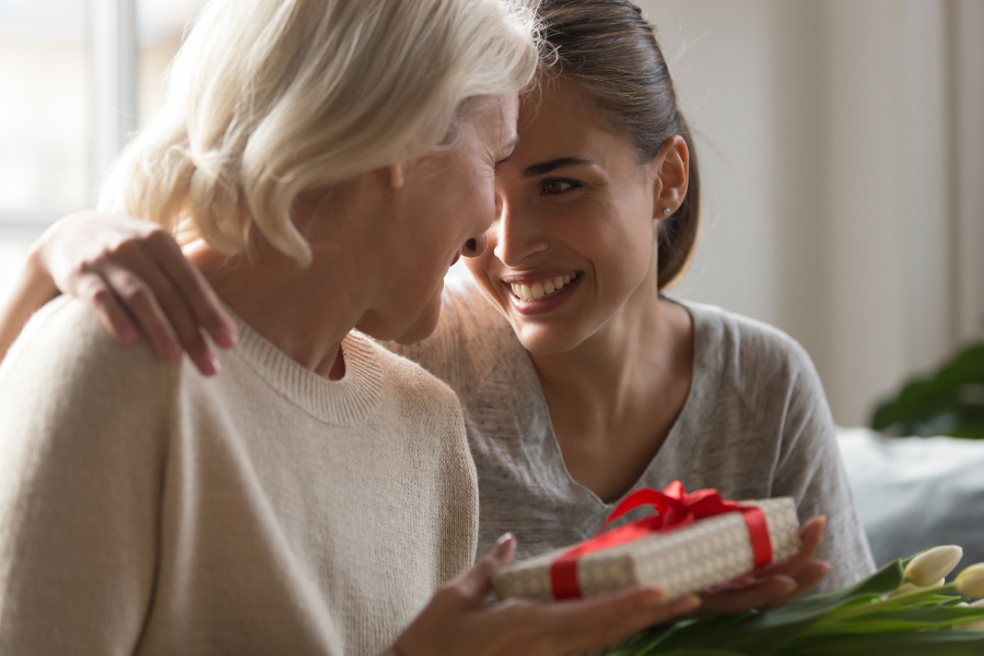 In a heartfelt moment, a younger woman embraces an older woman while giving her a gift, highlighting their deep connection and joy.