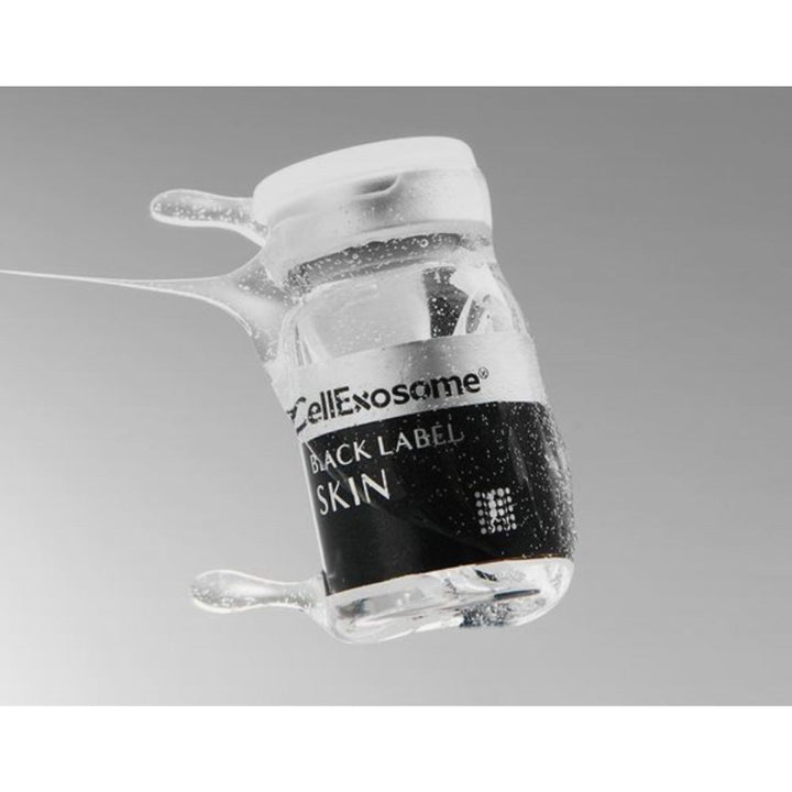 Close-up of a CellExosome BLACK LABEL Skin vial surrounded by serum droplets, highlighting the professional exosome skin regeneration treatment and premium skincare formulation.