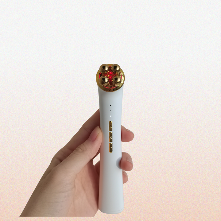 A hand holding a white and gold with white beauty tool 3-in-1 Luxe Microcurrent Under Eye Massager.