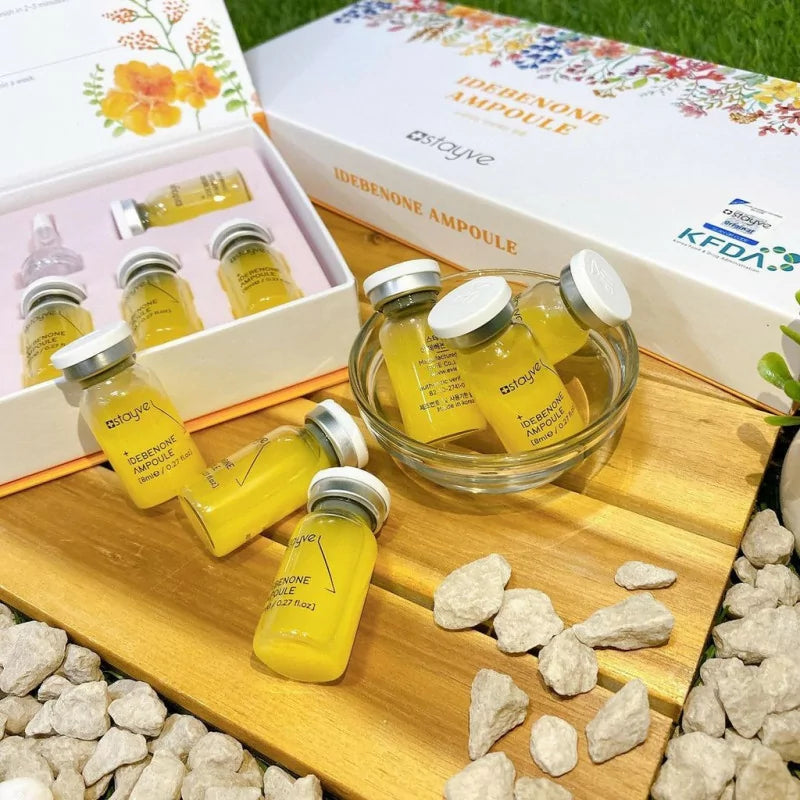 Stayve Idebenone Ampoule vials filled with yellow serum, displayed in a glass bowl and arranged on a wooden surface.